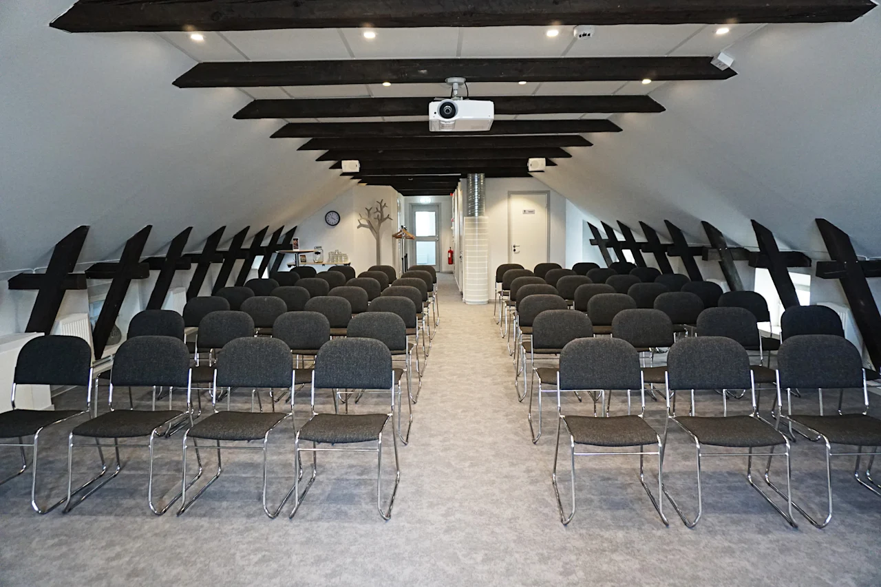 Ett modernt konferensrum med rader av stolar, en projektor och synliga takbjälkar, redo för en presentation.
