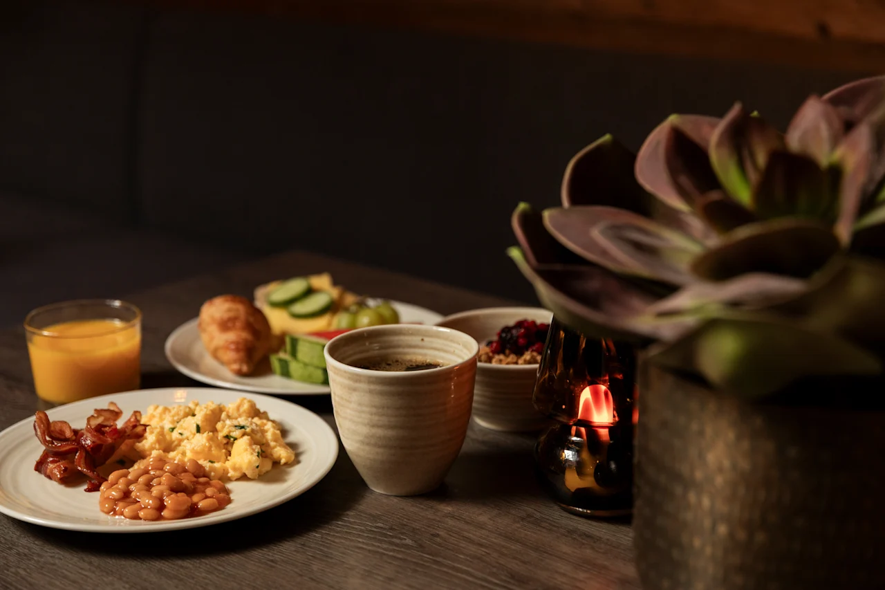 En varm og indbydende morgenmadsbuffet på et træbord, med et udvalg af retter, kaffe og appelsinjuice.