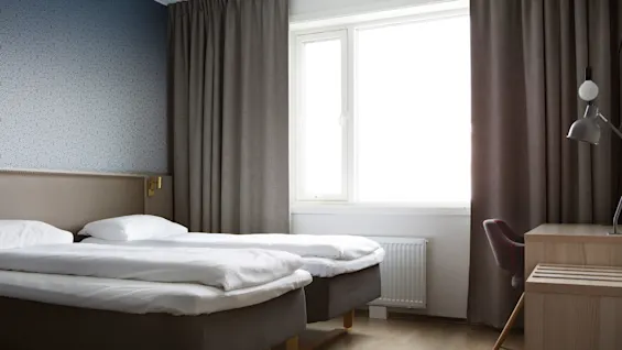 Two twin beds with white bedding in a neat hotel room, natural light from a window.