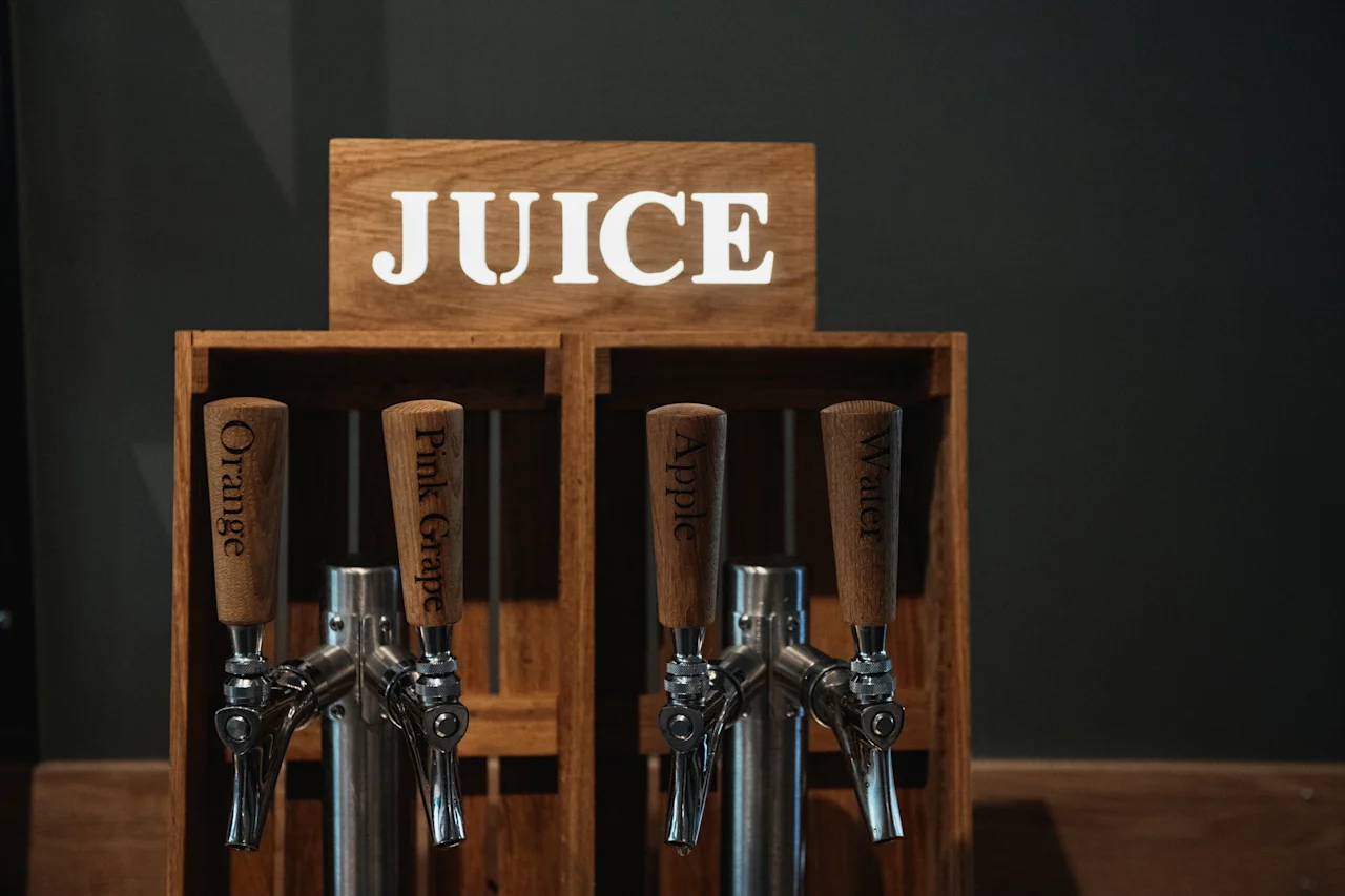 En självbetjäningsdryckesstation med en JUICE-skylt. Dispensrar erbjuder apelsin, rosa grapefrukt, äpple och vatten.