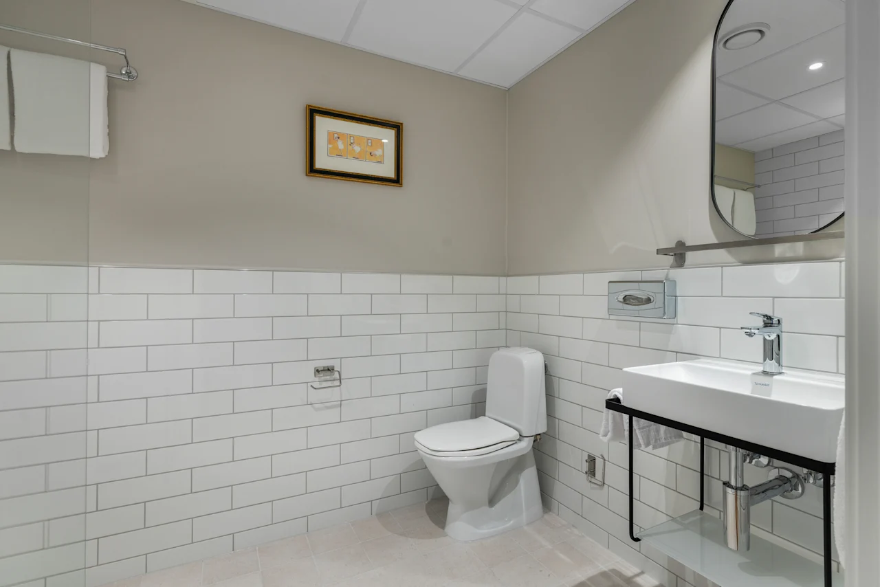 A clean and modern bathroom featuring white subway tiles, a toilet, a sink with a mirror, and fresh towels.