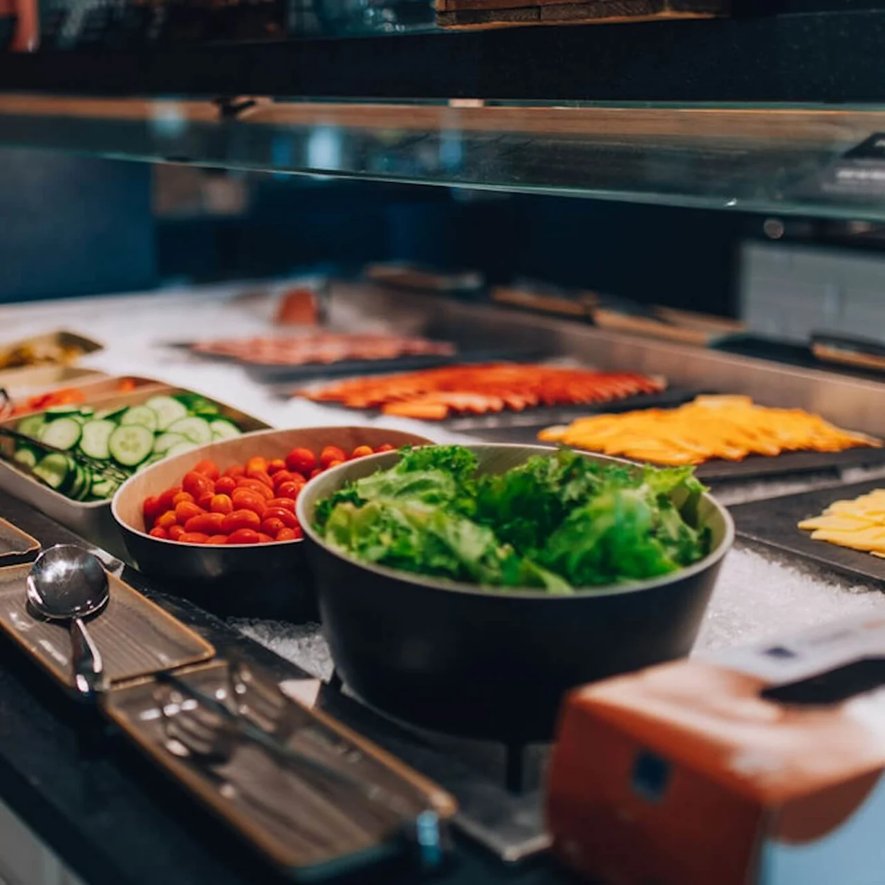Grøntsager og ost er arrangeret på en buffetdisk, omgivet af små tallerkener og bestik i en spisesammenhæng.