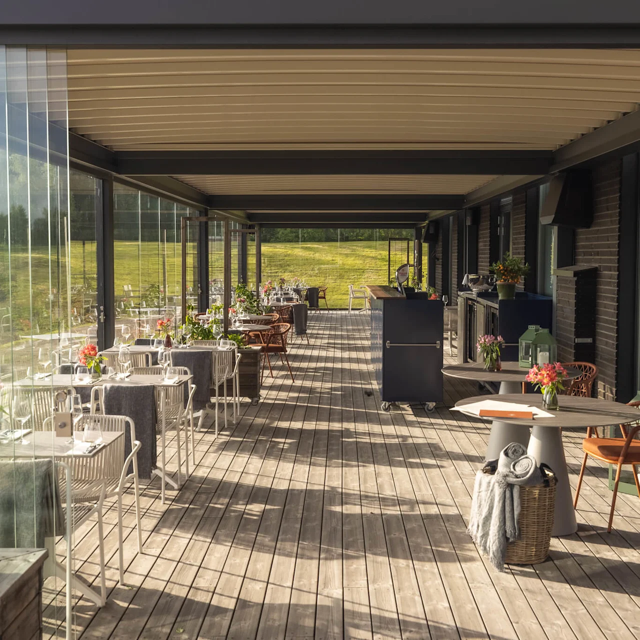 Utomhus matsalsområde med möbler på en träterrass, med utsikt över ett soligt, grönt landskap på Lily Country Club i norska Klöfta.