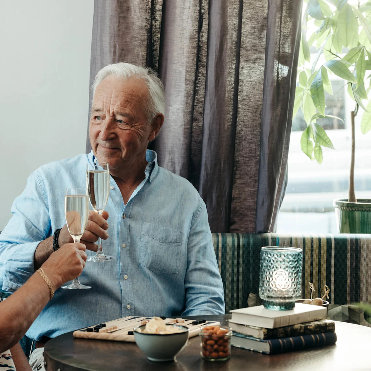 Two seniors toast with champagne indoors, smiling, with a cozy home setting.