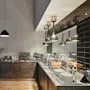 Buffet setup with covered dishes on a countertop, surrounded by industrial lamps. Plates and a bowl of eggs are neatly arranged. A chalkboard sign displays: "here, we have it all."