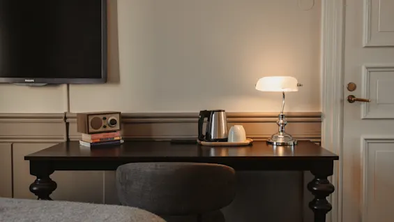 Ett mysigt hotellrums skrivbord med en lampa, vattenkokare, radio och TV, vilket antyder en bekväm vistelse.