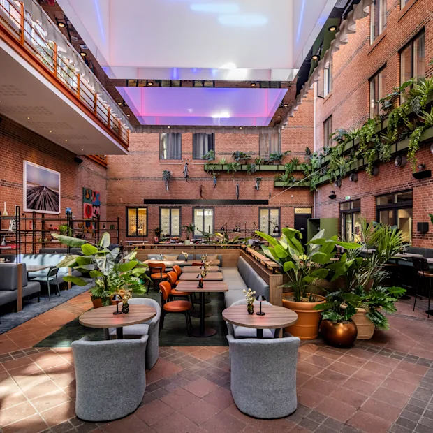 An inviting indoor courtyard at Comfort Hotel Vesterbro with dining tables, lush plants, and brick walls under a bright skylight.