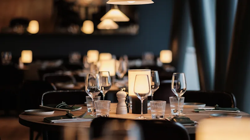 Dining table set with wine glasses and plates, surrounded by softly lit lamps in a dimly lit restaurant.