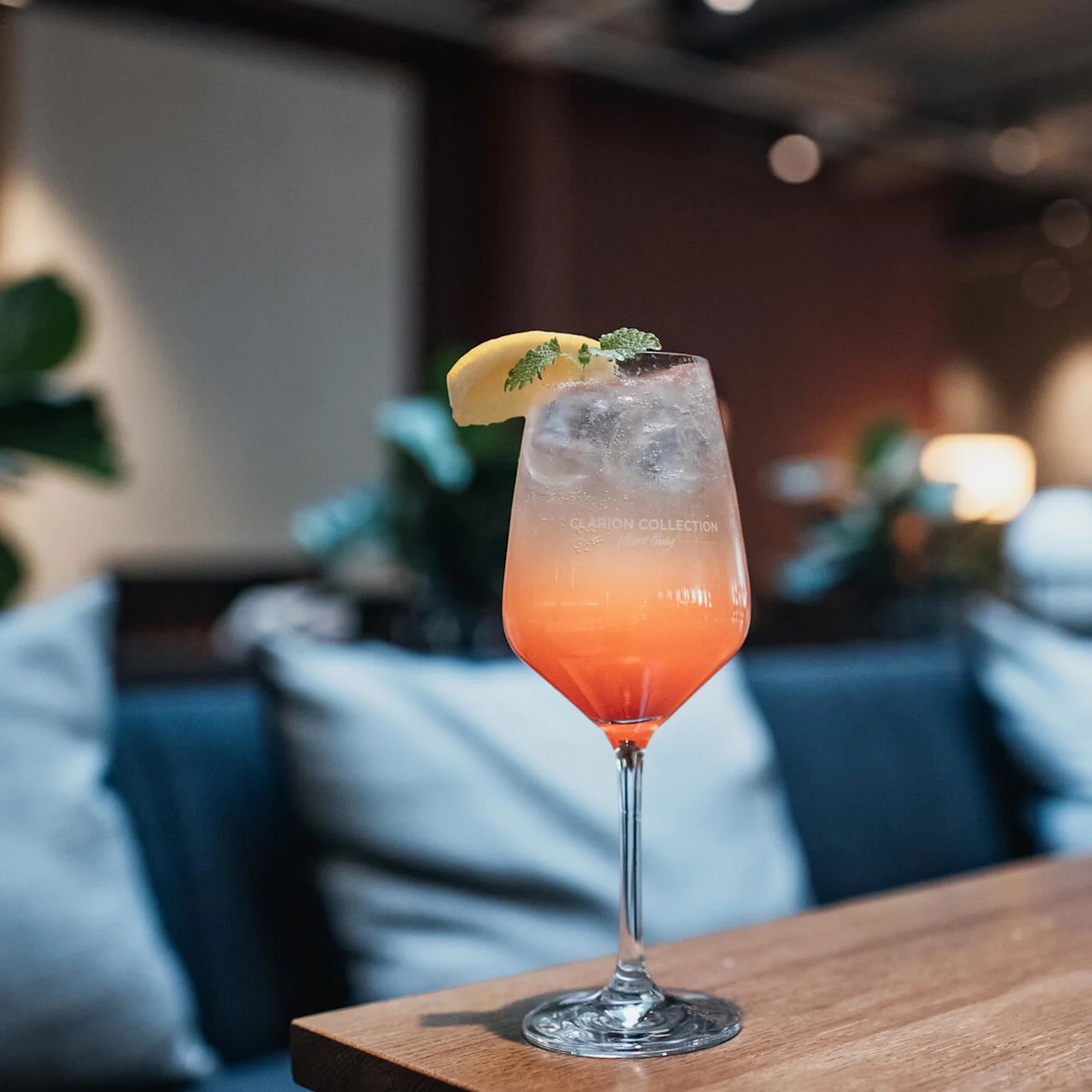A colorful cocktail stands on a wooden table with a blurred lounge setting in the background.
