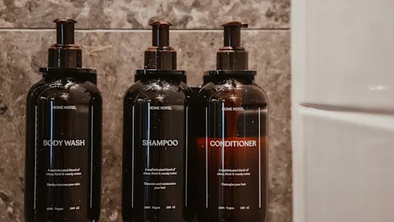 Tummat BODY WASH, SHAMPOO ja CONDITIONER -pullot suihkussa, tuoksuna sitrus, kukat ja puu.