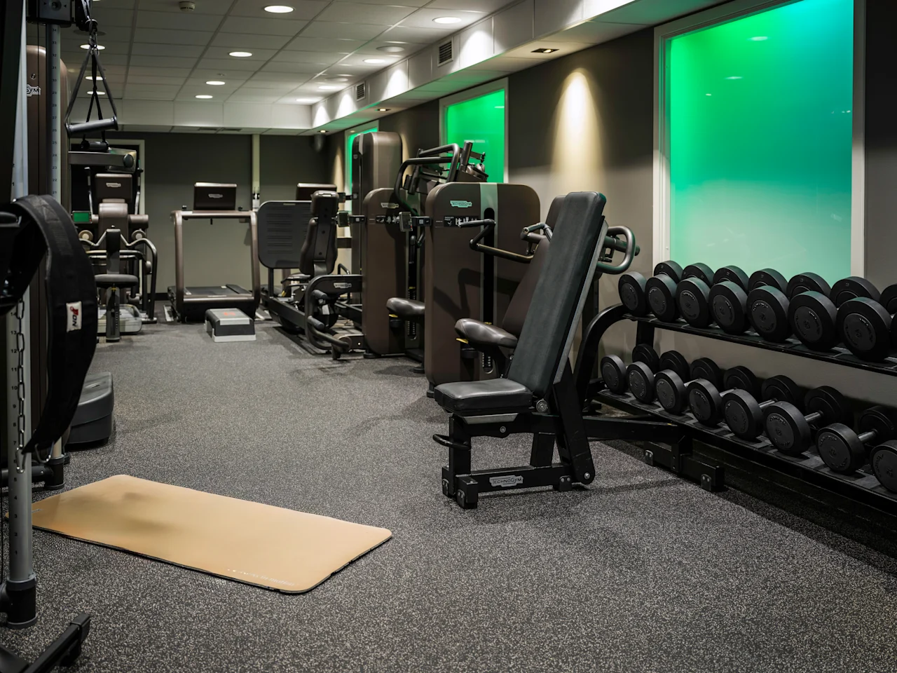 A well-equipped gym with various exercise machines, a rack of dumbbells, and a yoga mat on the floor, ready for a workout.