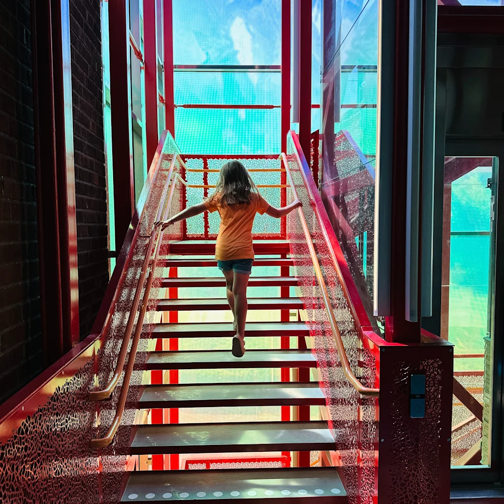 A person walks up a vibrant red and glass staircase at Vattenhallen Science Center i Lund, bathed in colorful light.