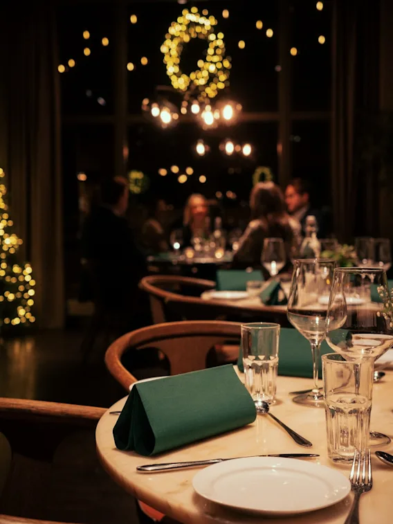 Dukat bord på en restaurang i mysig julbelysning med gäster som äter middag i bakgrunden.