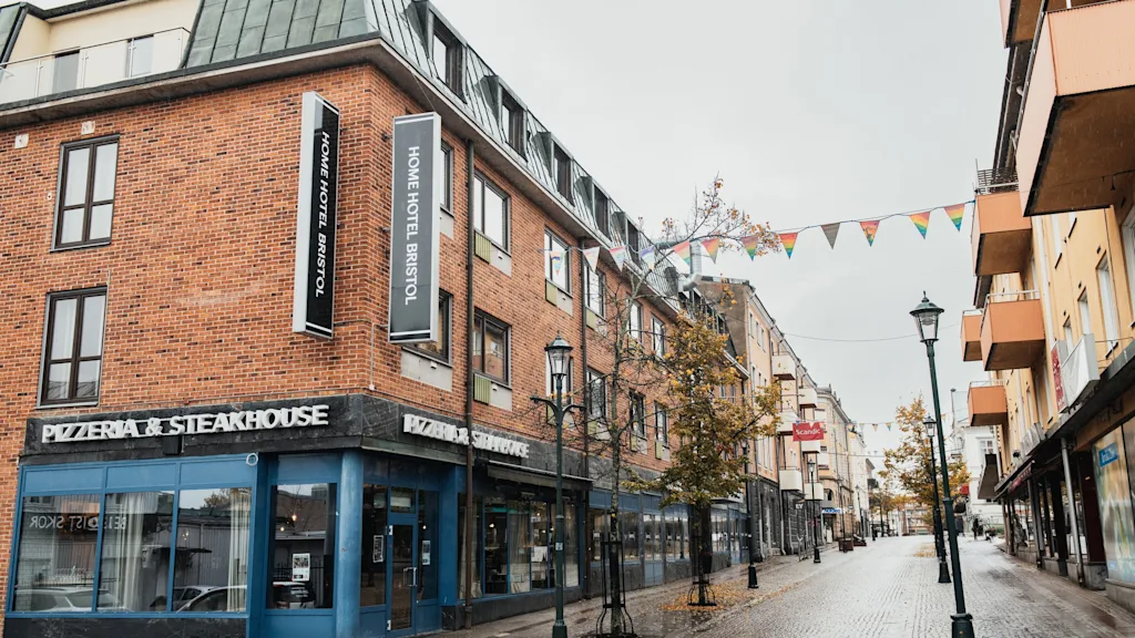 Katunäkymä tiilirakennuksella, jossa on hotelli ja ravintola. Värikkäät viirit roikkuvat märän mukulakivikadun yllä.