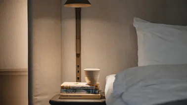 A cozy bedside scene at Home Hotel Victoria with a stack of books, a cup, and a warm lamp, inviting relaxation.
