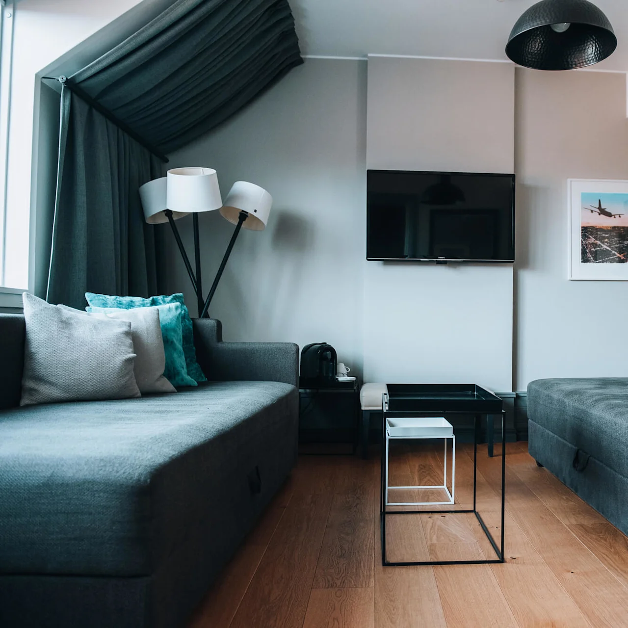 To grå sofaer med turkise puder er placeret over for hinanden i en moderne stue. Et sort TV er monteret på væggen over et lille glas sofabord.