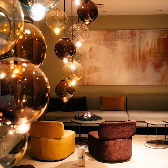Stemningsfull hotellounge med hengende glasskulelamper, behagelig sofa og myke fløyelsstoler i gult og vinrødt.