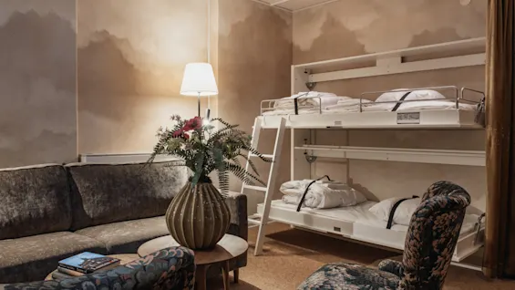 Home Hotel Baltzar - Family Room. A cozy hotel room with a sofa, patterned chair, and bunk beds, perfect for a family stay.