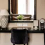 Et skrivebord med en svart stol og en lampe til venstre; en kaffemaskin og innrammet bilde til høyre. Stor speil reflekterer en sofa og bukett, som skaper en koselig atmosfære.