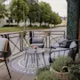 An inviting outdoor patio with comfortable seating and small tables, adorned with plants, next to a quiet street.