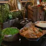 Ärter, paj och potatismos står under gyllene lampor på ett buffébord, omgivna av trälådor och färska örter, vilket skapar en mysig måltidsmiljö.