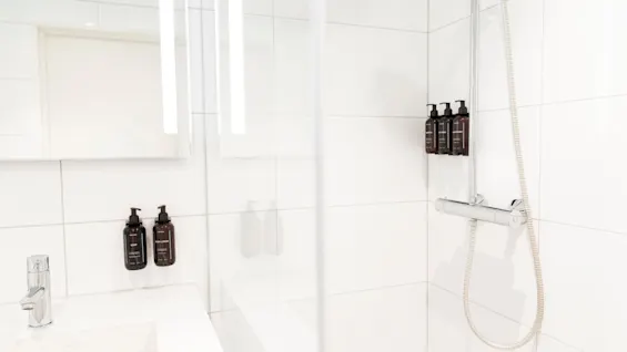 A modern bathroom at Home Hotel Grand Bodø with a shower and sink, featuring amenities like soap, body lotion, hair, body, and hand wash.