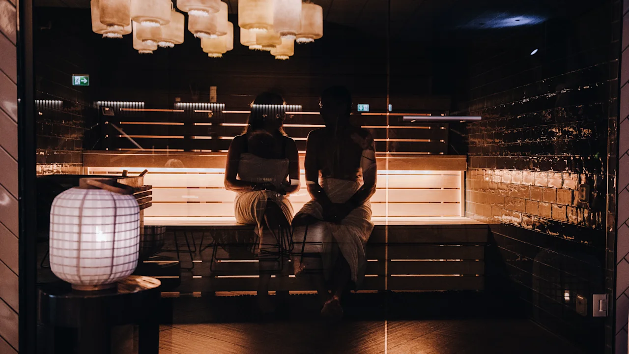 Två personer kopplar av i en dämpat upplyst bastu och njuter av en stunds lugn och värme.