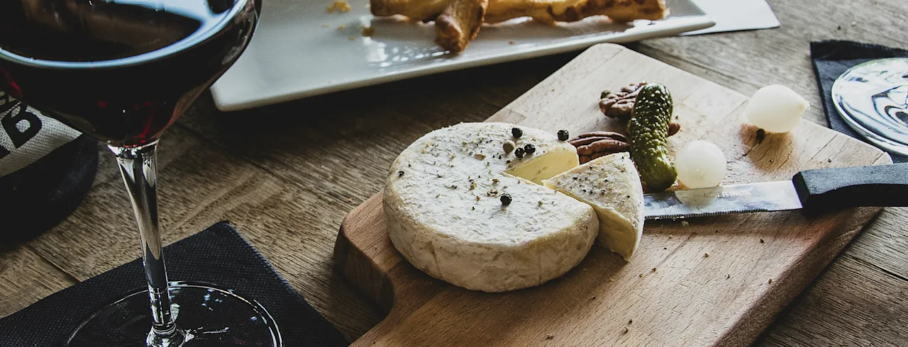 Nautitaan herkullisesta punaviinistä, juustosta, pähkinöistä ja suolakurkuista rustiikkisella puupöydällä.