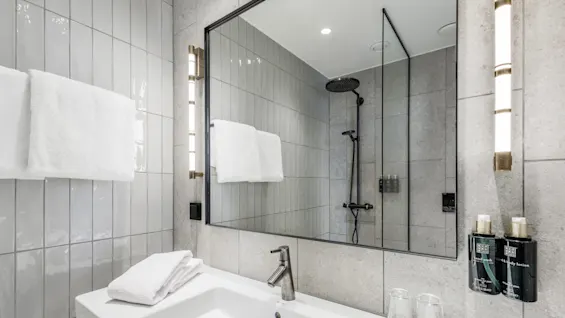 A modern bathroom with a reflective mirror above a sink, adjacent to a glass-enclosed shower.