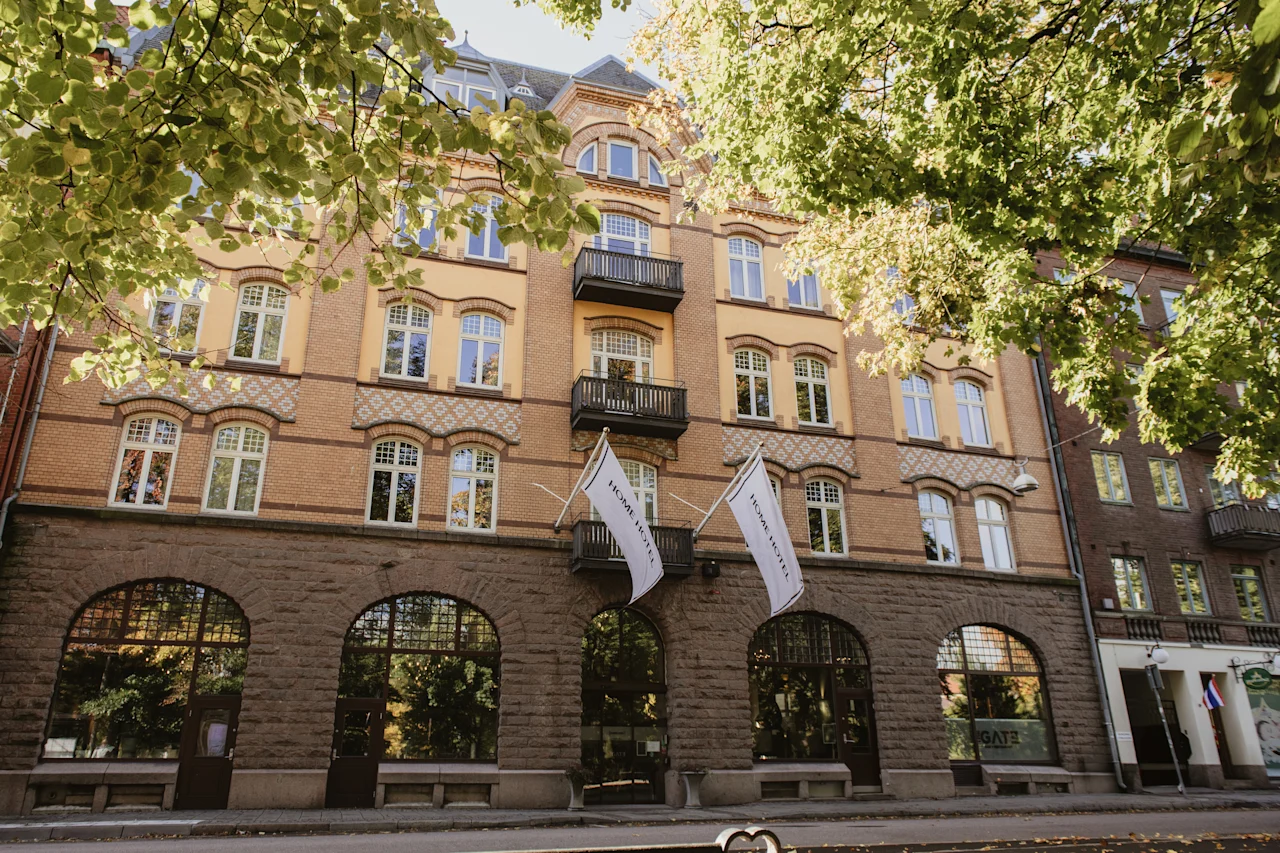 Home Hotel Norre Park in Halmstad, a charming building with flags, framed by green trees on a sunny day.