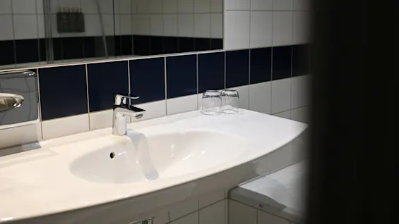 Ett badrumshandfat med en blank kromkran står mot en vägg med vita och mörkblå kakelplattor. Två uppochnervända glas står på bänkskivan.