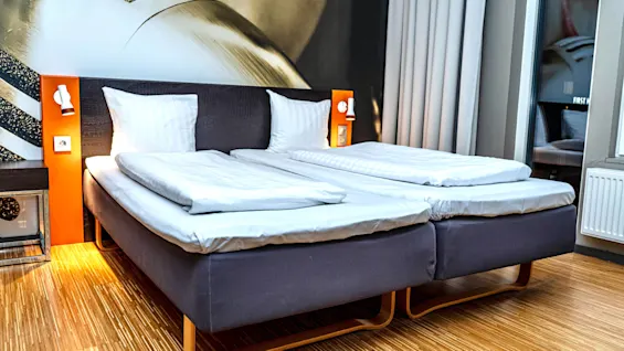A modern hotel room with two beds, bedside lamps, and wooden flooring. 