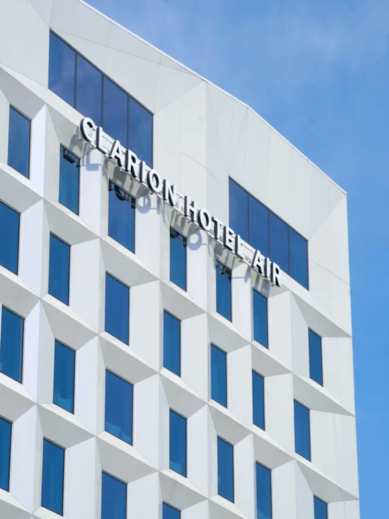 A modern white building facade with geometric windows, displaying the text "CLARION HOTEL AIR" against a clear blue sky.
