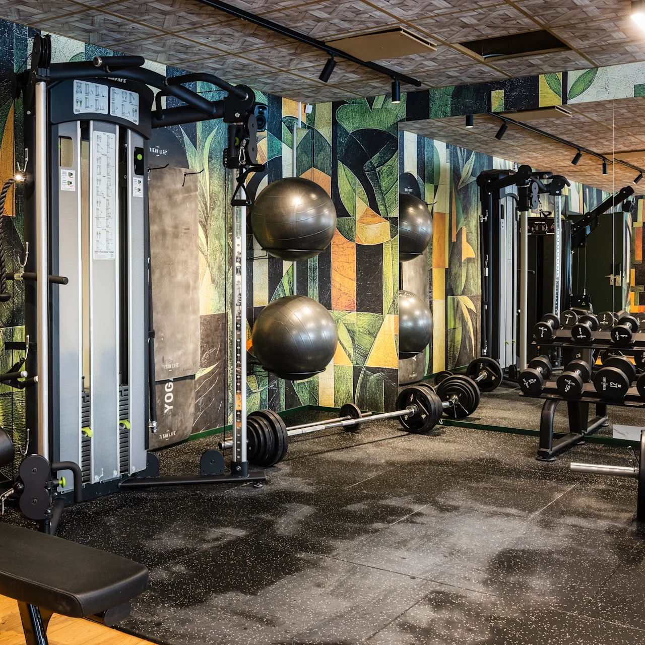 Gym equipment, placed in a modern gym setting, includes dumbbells on racks, weight machines, and exercise balls against a colorful geometric-patterned wall, creating an energetic workout atmosphere.