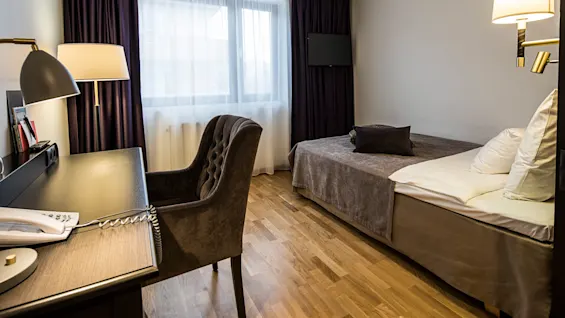 A neatly arranged hotel room with twin beds, a desk, chair, and lamps.
