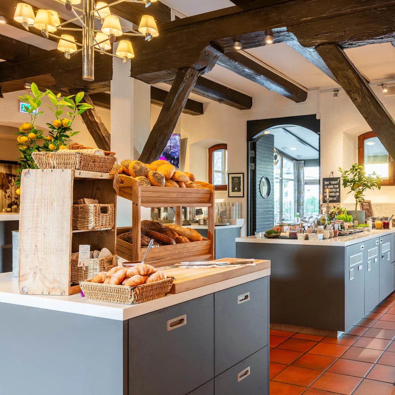 A bakery counter displays various breads and pastries in a rustic room with wooden beams and a tiled floor.