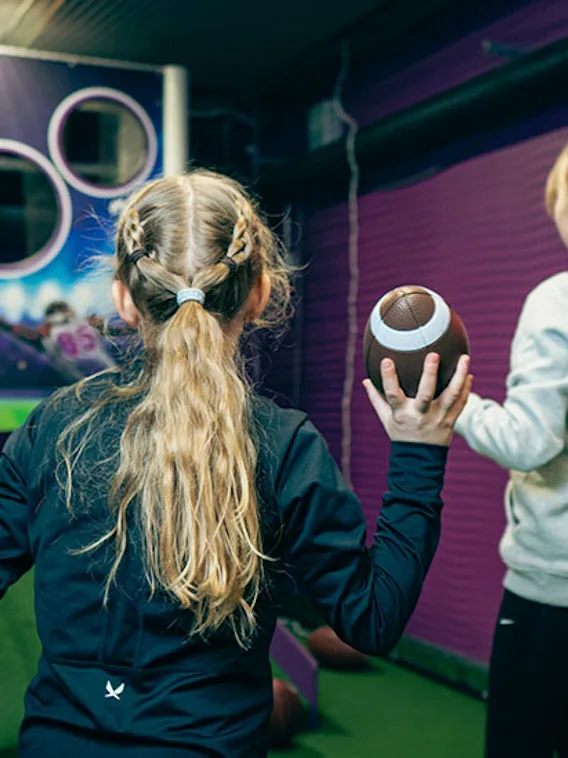 Kaksi lasta pelaa sisäjalkapallopeliä. Toinen pitää palloa ja katsoo maalitaulua, jossa on ympyrät ja 20.