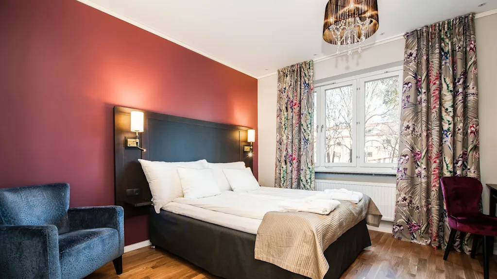 A well-lit bedroom with a large bed, accent armchairs, and colorful curtains, showcasing a harmonious blend of warm and cool tones.