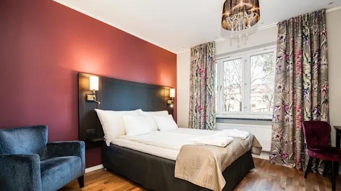 A well-lit bedroom with a large bed, accent armchairs, and colorful curtains, showcasing a harmonious blend of warm and cool tones.