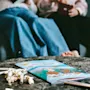Coloring book with cartoon animals lies open on a marble table, surrounded by scattered popcorn and pencils. Two people sit on a sofa in the background.