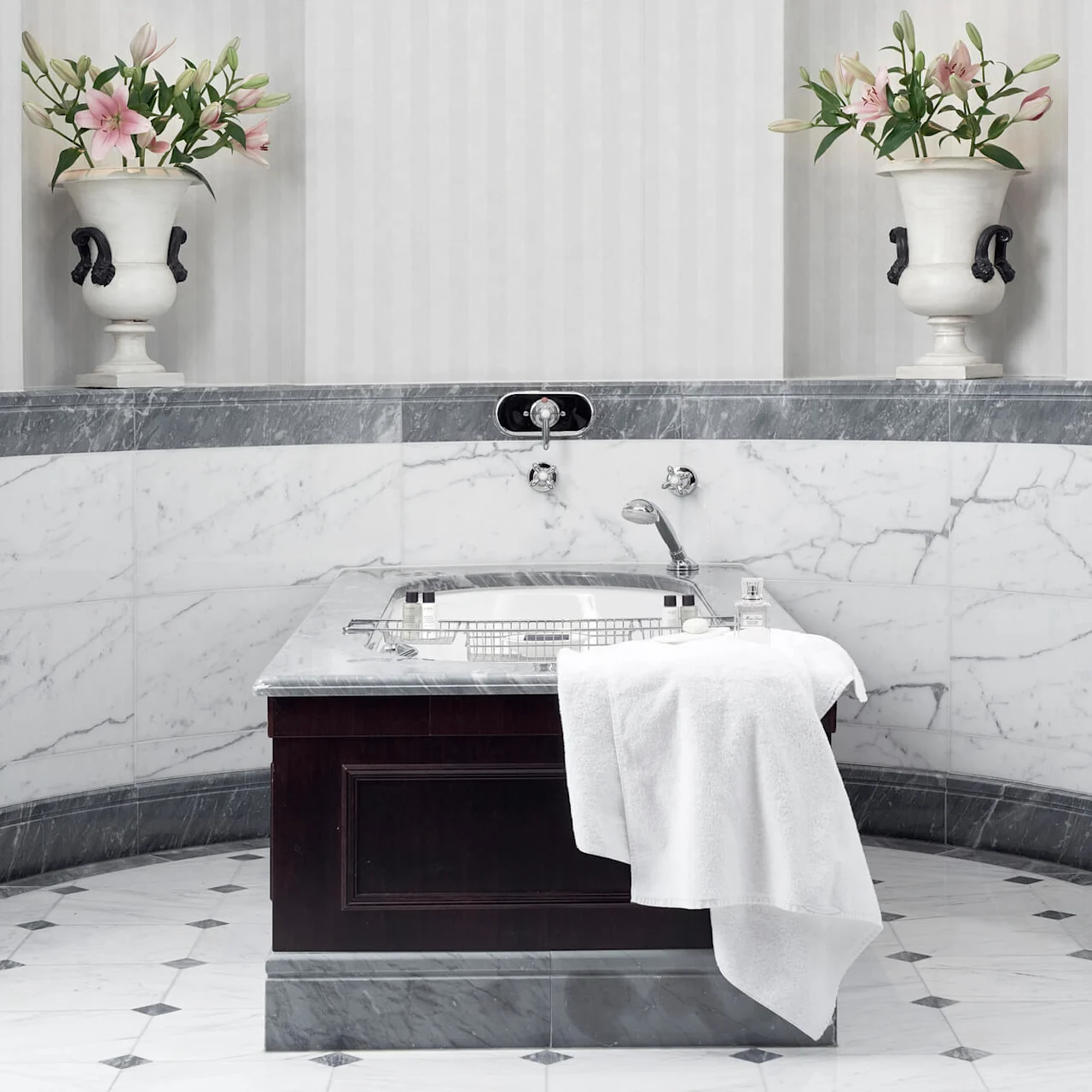 Elegant bathroom sink with flowers in a vase, set against marble and striped wallpaper, providing a sophisticated ambiance.