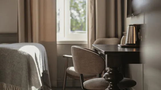 Ett lugnt hotellrum med en bekväm säng och en välutrustad skrivbordsplats, upplyst av mjukt naturligt ljus.