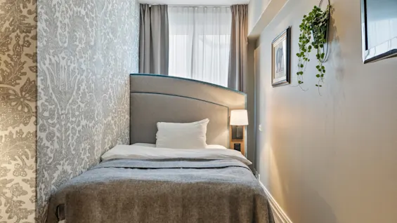 A cozy hotel room with a single bed, patterned wallpaper, and soft lighting, creating a comfortable and inviting atmosphere.