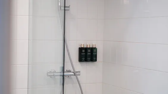 En ren, moderne dusj med hvite fliser, en glassvegg og veggmonterte dispensere for toalettartikler.