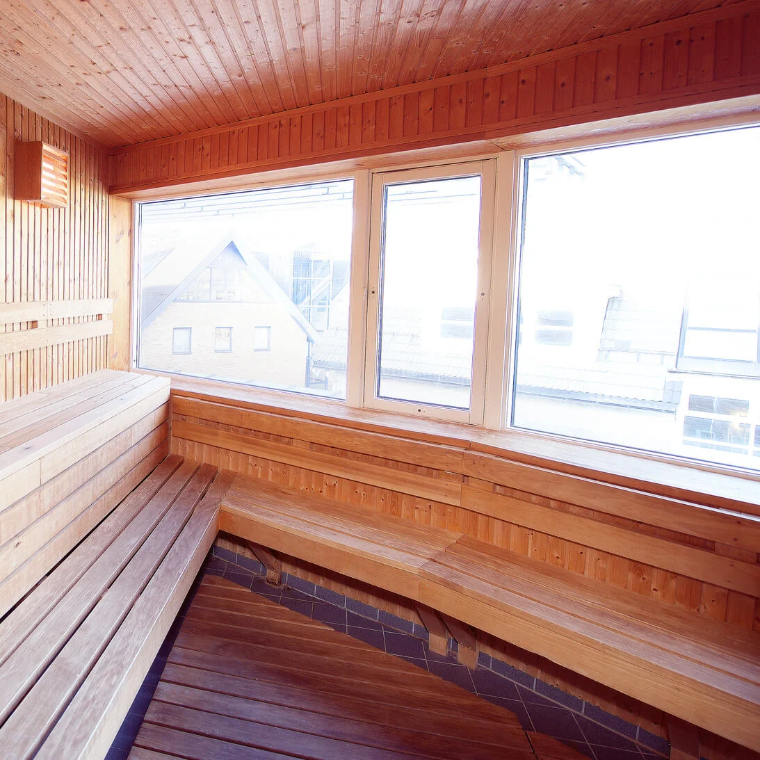 A wooden sauna with benches, a heater and a window offering a view outside.