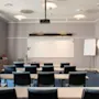 Et moderne konferencelokale med rækker af borde og stole vendt mod en whiteboardtavle og projektor, klar til en præsentation eller et møde.