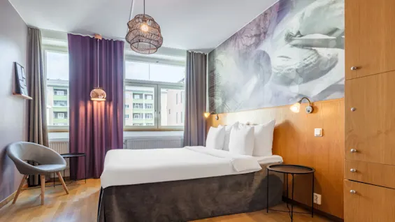 A well-lit modern bedroom with a double bed, wooden furniture, and purple curtains, in an urban apartment setting.