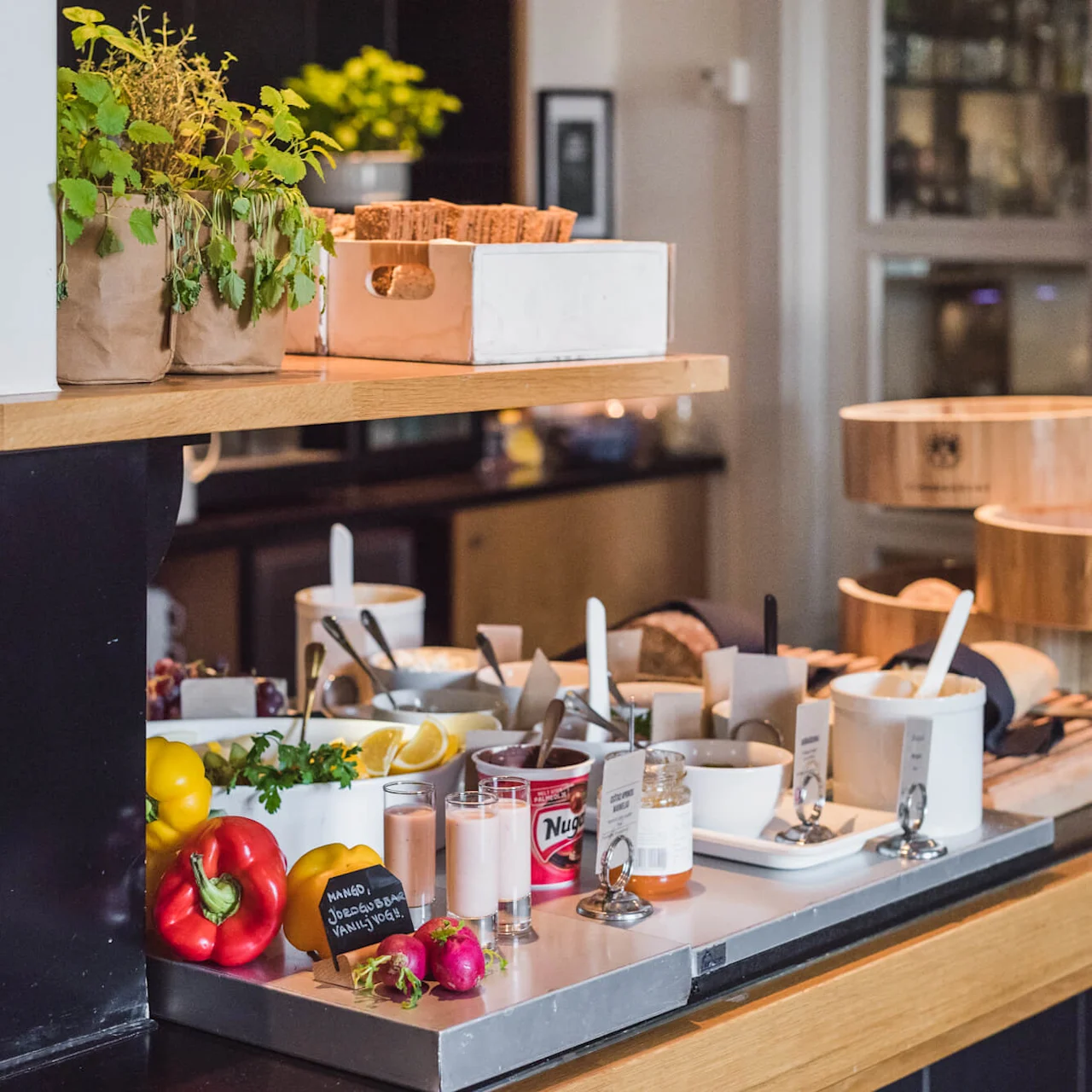 A breakfast buffet setup with assorted foods and condiments on a wooden table, in a cozy room with shelves.