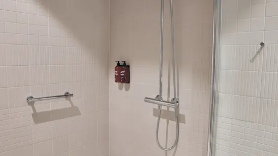 Ett rent, kaklat duschutrymme med duschhuvud, handdukstork och väggmonterade dispensrar för schampo och tvål.