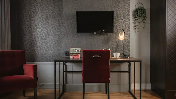 En inbjudande arbetsplats i ett hotellrum på Home Hotel Grand, Helsingborg, med ett skrivbord, röd stol och väggmonterad TV.